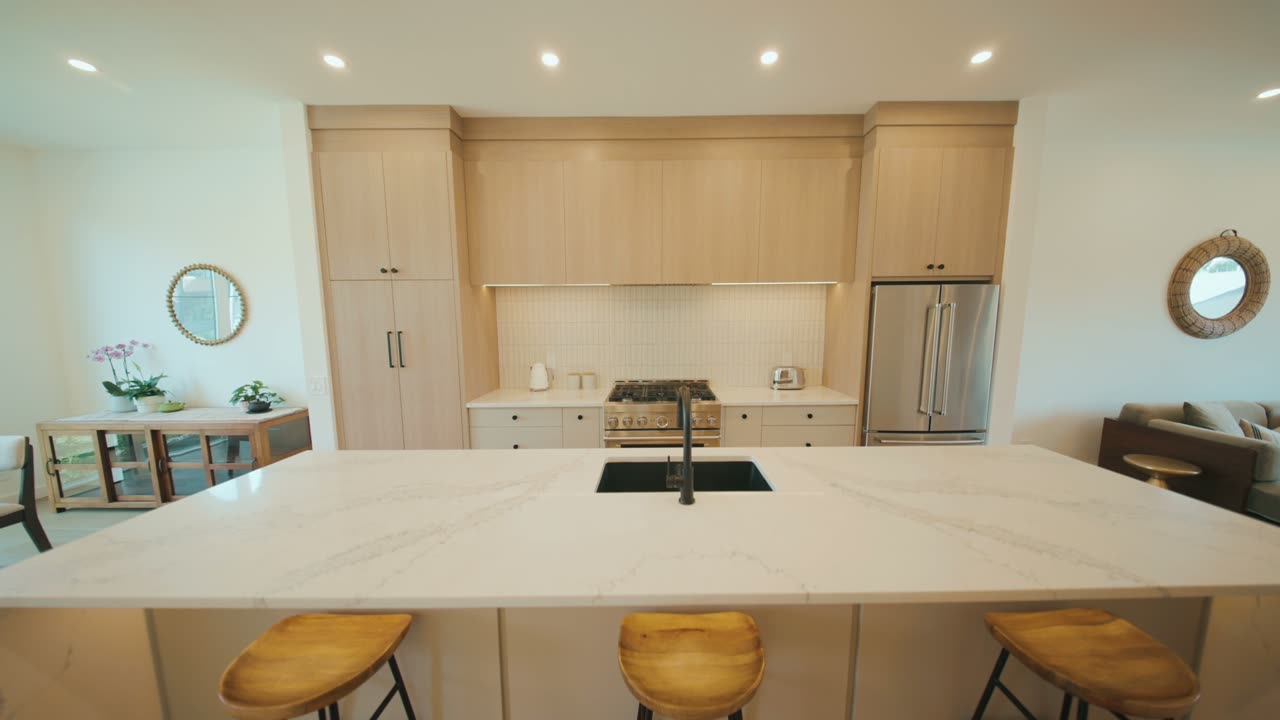 Listing film still: kitchen with a marble island, light oak cabinets and wood stools